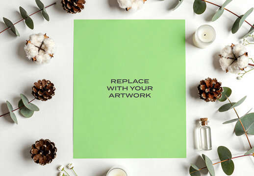 Vertical paper mockup displayed on a white surface surrounded by eucalyptus branches, pinecones, cotton bolls, candles, and small glass bottle, design