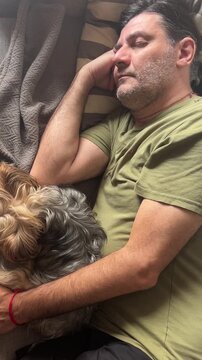 Serene moment of a mature man and his small yorkshire terrier dog sleeping together on the couch, illustrating a beautiful connection, relaxation, and peacefulness in a comfortable home