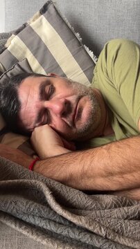 Mature man sleeping soundly on the sofa at home, taking a peaceful nap while breathing calmly to recover his energy after a long and stressful day