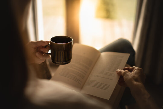 Person at home relaxing with feet up by the window reading and enjoying a morning cup of coffee	