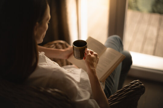 Woman at home relaxing by the window reading and enjoying a morning cup of coffee	