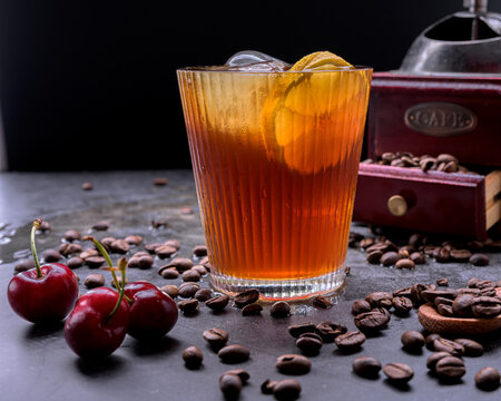 Refreshing iced coffee cocktail with orange slice ice cubes vintage manual grinder and scattered roasted coffee beans on dark surface
Keywords