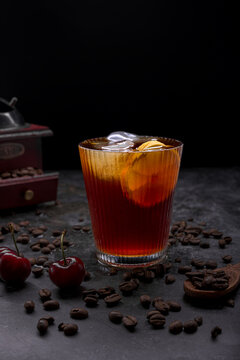Refreshing iced coffee cocktail with orange slice ice cubes vintage manual grinder and scattered roasted coffee beans on dark surface
Keywords