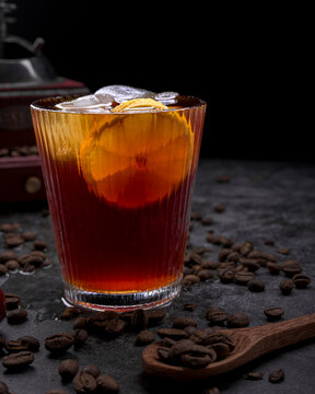 Refreshing iced coffee cocktail with orange slice ice cubes vintage manual grinder and scattered roasted coffee beans on dark surface
Keywords