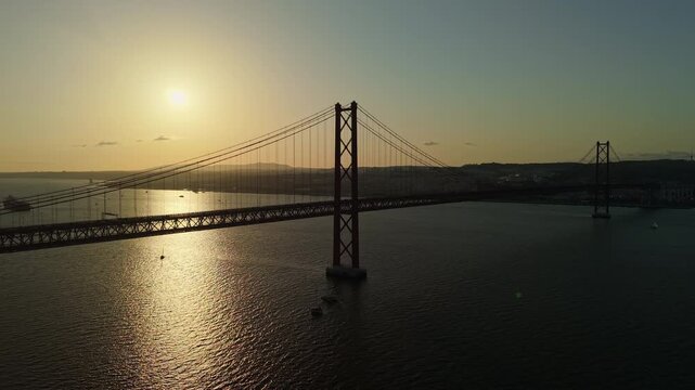 Aerial view of the 25 de Abril suspension bridge silhouetted against a golden sunset over the Tagus River near Lisbon, Portugal