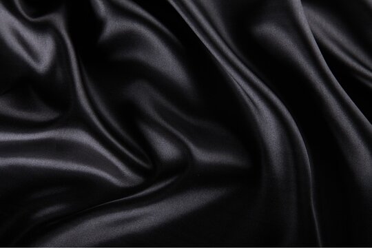Black silk fabric texture with elegant folds and smooth satin waves for luxury background