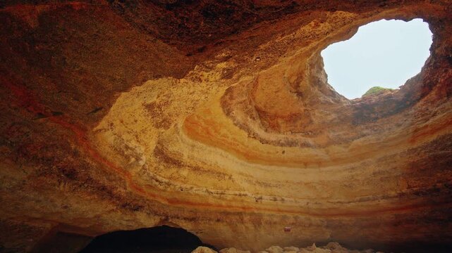 Layered limestone walls, sandy beach and natural ceiling opening inside the famous Benagil Cave in Algarve.