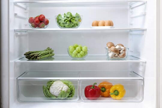 Fresh vegetables and eggs organized in refrigerator for healthy lifestyle. Assorted vegetables include asparagus, lettuce, and peppers alongside fresh eggs for nutritious meals.
