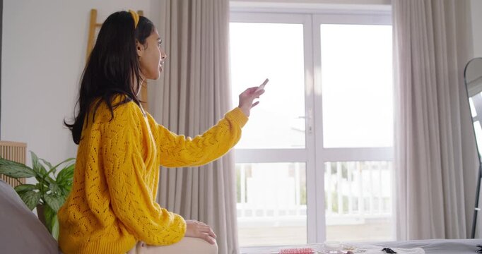 Two female friends sitting on bed one entering with rust bag passing lipstick and playfully dancing