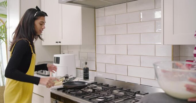 Indian woman receiving mixing bowl, oiling pan, stirring batter and pouring pancakes at gas range