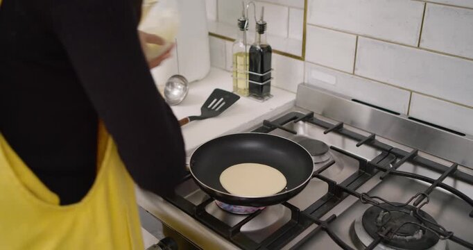 Wooden spoon is spooning pale batter into preheated nonstick pan on gas stove for breakfast