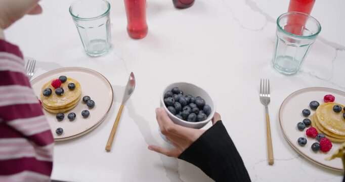 Pointing at pancakes is starting hands topping plates with berries and syrup at table to eat