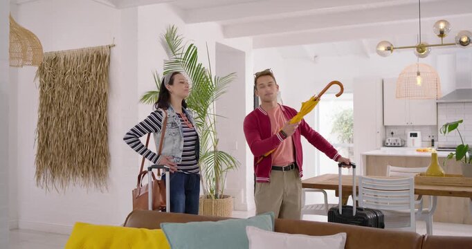 Couple arriving, pulling suitcases and umbrella into rental home, inspecting layout while orienting