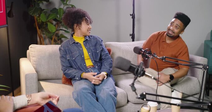 African American hosts woman denim man rust polo turning gesturing to applause in studio taping mic