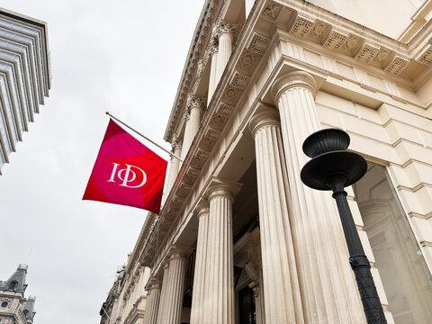 Historic neoclassical building with grand columns and a red Institute of Directors IoD corporate flag in London, UK