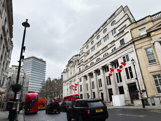 Fototapeta premium Red buses and Canadian flags along a classical city street in London, UK with overcast sky
