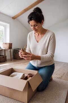 Woman unboxing new minimalist decor items from cardboard box at home, showcasing a minimalist lifestyle. The minimalist lifestyle promotes decluttering and embracing simplicity,