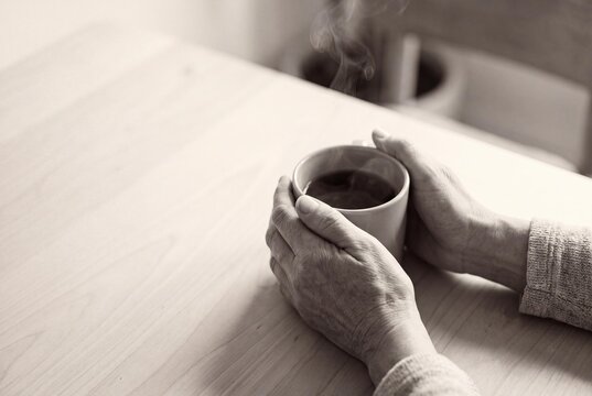 Two hands gently interlace around a warm ceramic cup with steam