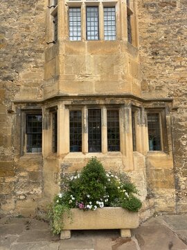 Historic Cotswold stone building facade with mullioned windows and planter in English village