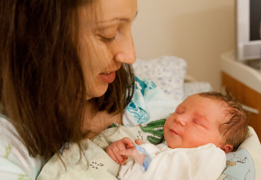 Mother and her newborn baby boy in bed in hospital. Baby sleeping in her hands