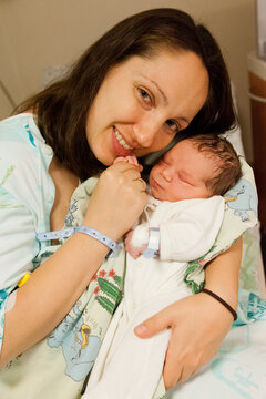 Mother and her newborn baby boy in bed in hospital. Looking at the camera