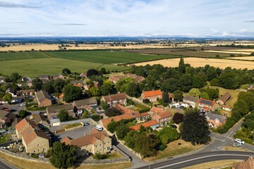 Fototapeta premium Aerial photo overlooking traditional homes near Thirsk Yorkshire surrounded by expansive agricultural fields mature trees country roads and rolling North Yorkshire countryside in the distance