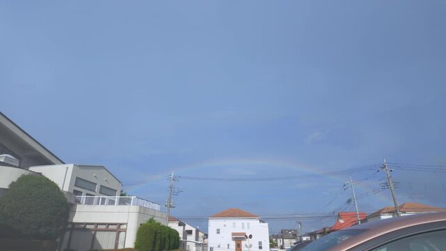 Beautiful rainbow in the blue sky over a peaceful residential neighborhood during a sunshower