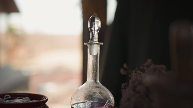 Clear glass decanter with round stopper stands on interior table, glowing in warm backlight with soft reflections, shallow depth of field, elegant curves, quiet natural window light and calm mood