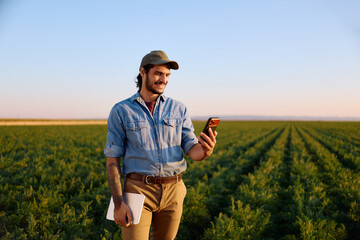 Happy agronomist using app on cell phone while standing in field. © Drazen