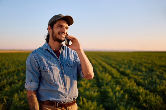 Young happy farmer communicating on cell phone in agricultural field.