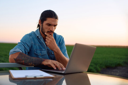 Pensive agronomist using laptop while working in field.