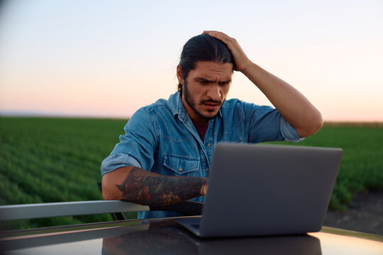 Worried farmer working on laptop in agricultural field.