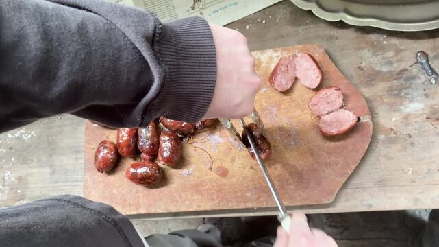 Slicing grilled chorizo sausages on a rustic wooden board for traditional Argentine barbecue, asado, classic food. Choripan, parrilla. 