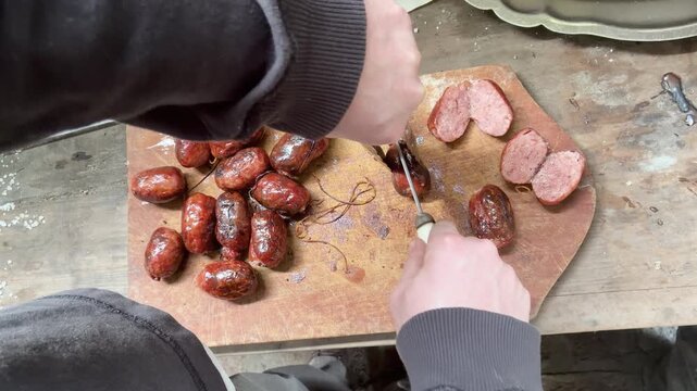 Close up of slicing roasted chorizo sausage on wooden board to prepare classic Argentine choripan, traditional Asado Argentino, parrilla, barbecue. 