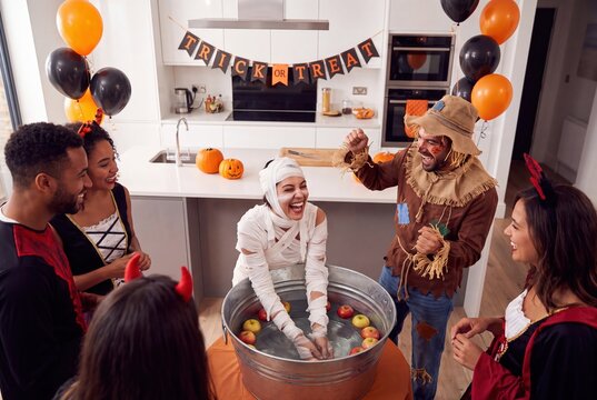 Friends in Halloween costumes playing apple bobbing game at home party