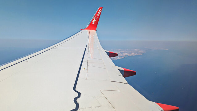 Passenger airplane wing above Malta coastline and blue Mediterranean Sea, clear sky and scenic aerial island view from window during daytime flight: Luqa, Malta-August 8, 2025