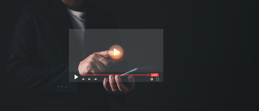 Businessman holding smartphone and touching a glowing virtual video player interface. Concept of live streaming, online broadcasting, multimedia content, digital entertainment, and interactive media.