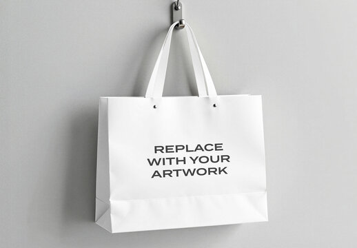 Paper shopping bag mockup hanging on a metal hook against light gray wall, blank front panel with text placeholder for branding, minimalist retail packaging design, commercial product display