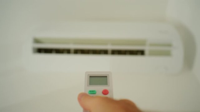 Hand holding a remote control, adjusting the temperature on a modern air conditioning unit for optimal climate control and comfort