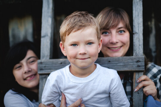 Portrait of a smiling young boy with his mother and sister framed by a rustic wooden window outdoors