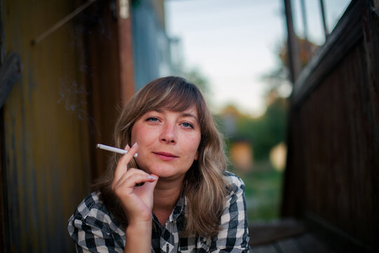 Portrait of a woman smoking a cigarette outdoors and looking at the camera in soft natural light
