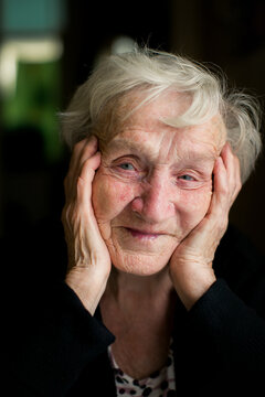 Close up portrait of a smiling senior woman holding her face in her hands at home