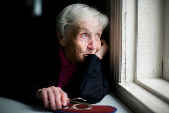 Thoughtful senior woman looking out a window at home in soft natural light