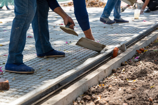 Construction worker smoothing mortar finish on a sidewalk edge using hand trowel tools