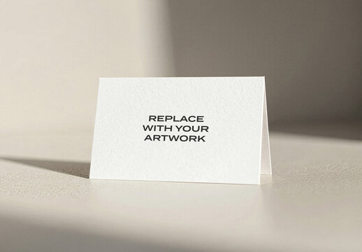 Folded paper card mockup standing upright on a textured surface, minimalist stationery presentation with soft lighting and natural shadows, design