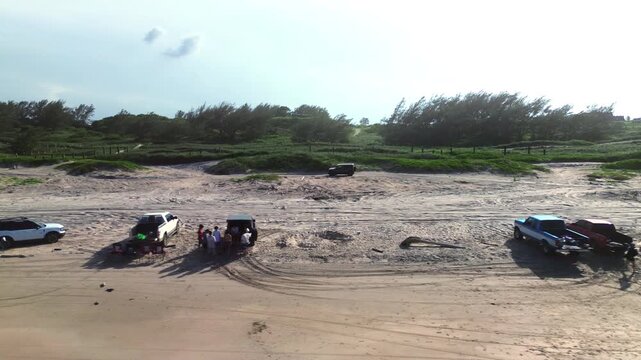 Off road vehicle crosses golden beach dunes at sunset, moving from left to right as the camera follows its path. Miramar Beach on the Gulf of Mexico provides a tropical setting with green coastal vege