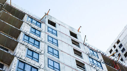 Apartment building under construction with unfinished facade and installed windows during the development of a modern residential complex © belavinstock
