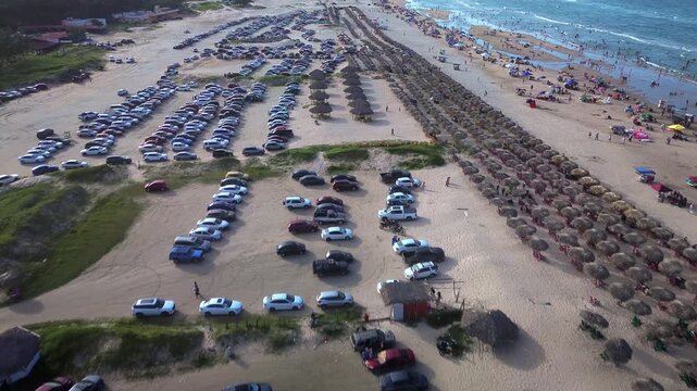 Miramar Beach parking area crowded with vehicles, beachgoers and palapas along the busy Gulf of Mexico shoreline