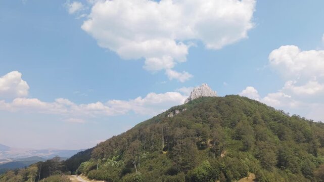 Aerial View of Drone Approaching Forested Hill with Rocky Peak Under Blue Sky and White Clouds, Visocica Mountain, Bosnia and Herzegovina