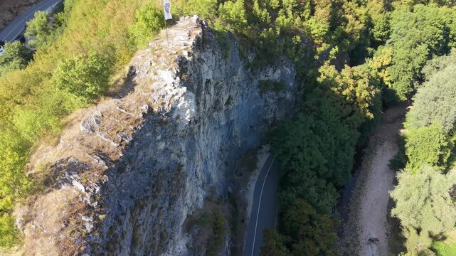 Aerial Flyover of Rock Face with Fleur-de-Lis Flag Above Dariva Showing Road, Miljacka River, and Climbers Below, Sarajevo, Bosnia and Herzegovina
